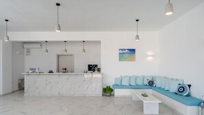 Un área de recepción moderna con un mostrador de mármol, una zona de estar con un sofá azul e iluminación colgante.