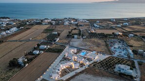 Vista aérea de un pueblo costero con edificios blancos, una piscina y campos.