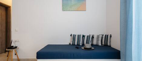 A bedroom with a bed, a small table, a chair, a hat, and a painting of a beach.