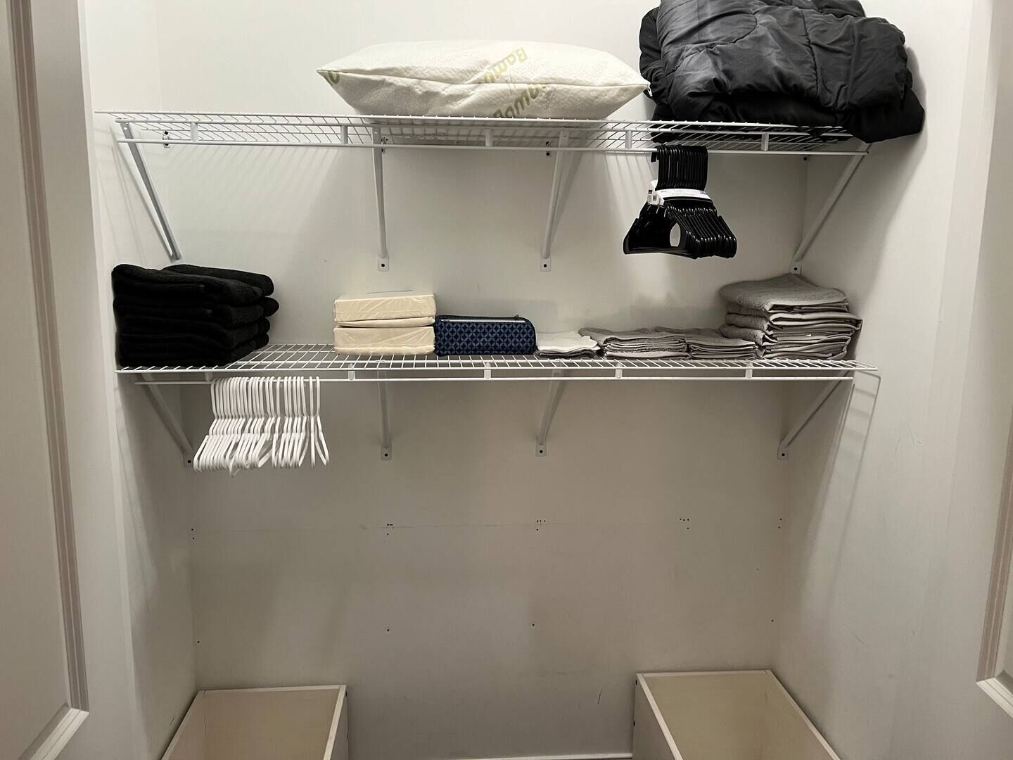 Ein Schrank mit Regalen, in denen gefaltete Kleidung, ein Kopfkissen und eine schwarze Tasche aufbewahrt werden.