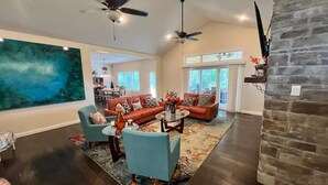 A spacious living room with a large painting, a stone fireplace, and a dining area visible in the background. - The Lighthouse- A Beautiful and Luxurious SmartHome. (Terre Haute)