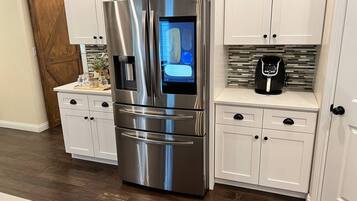 A stainless steel refrigerator with a digital display, white cabinetry, and a coffee maker on the countertop.