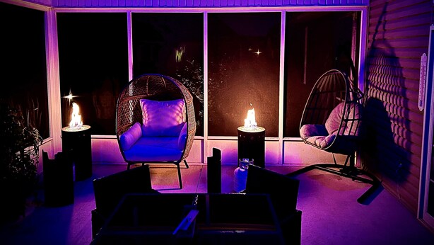 A cozy outdoor seating area with wicker chairs and a table, illuminated by two candles. - The Lighthouse- A Beautiful and Luxurious SmartHome. (Terre Haute)