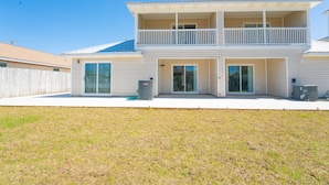 A two-story house with a balcony, large windows, and a grassy yard.