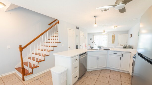 A modern kitchen with white cabinetry, a stainless steel refrigerator, and a wooden staircase.