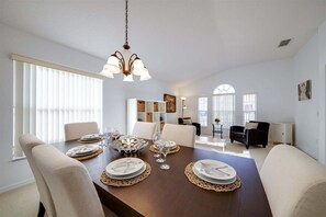 A dining area with a wooden table set for four, a chandelier, and a view of the living room. - 630 - Great 3 Bed 2 bBath Villa With Private South Facing Pool (Davenport)