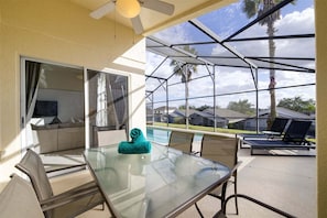 A glass-enclosed patio with a pool, outdoor seating, and a view of houses and palm trees.