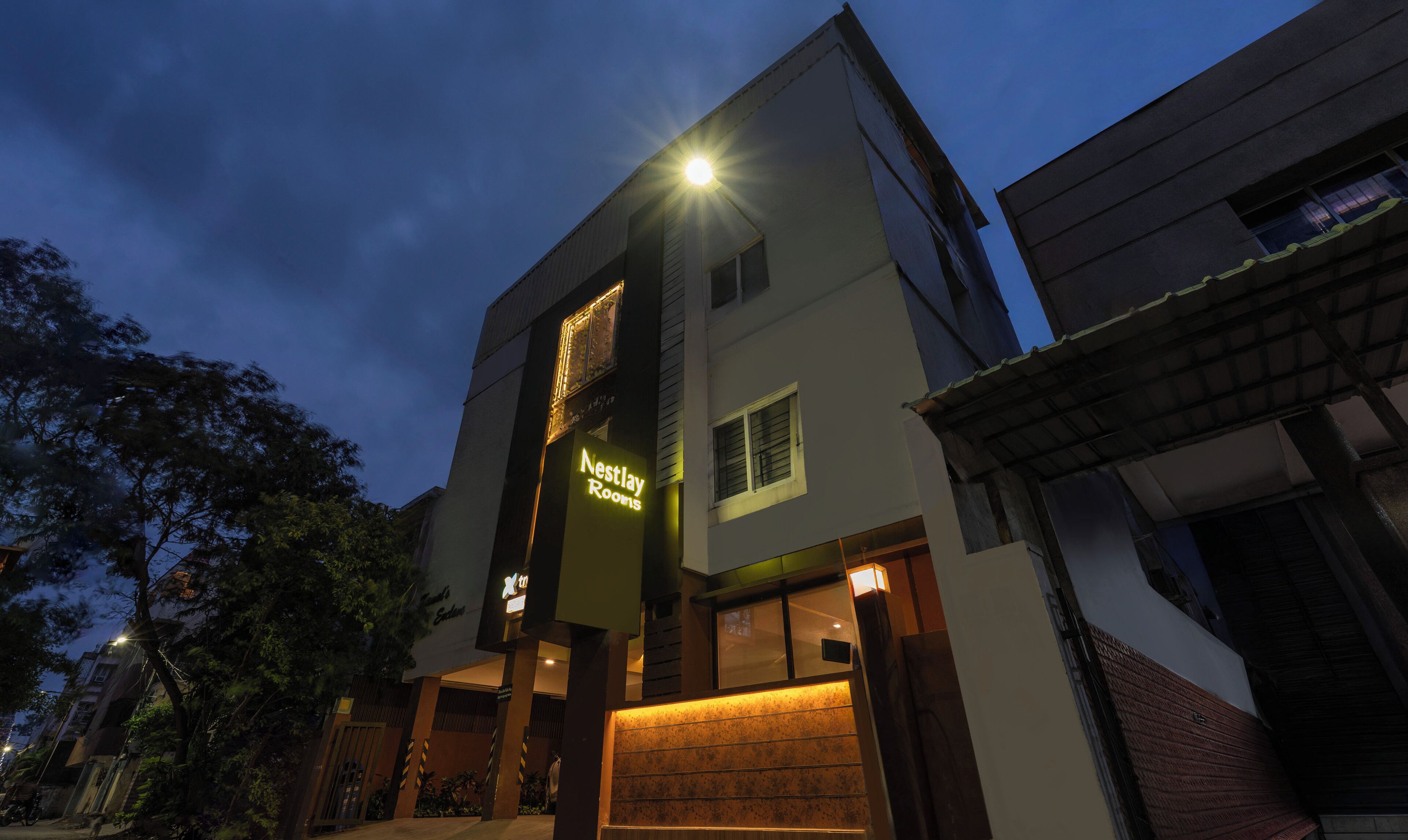 A multi-story building with a sign for 'Nestlay Rooms' and a well-lit entrance.