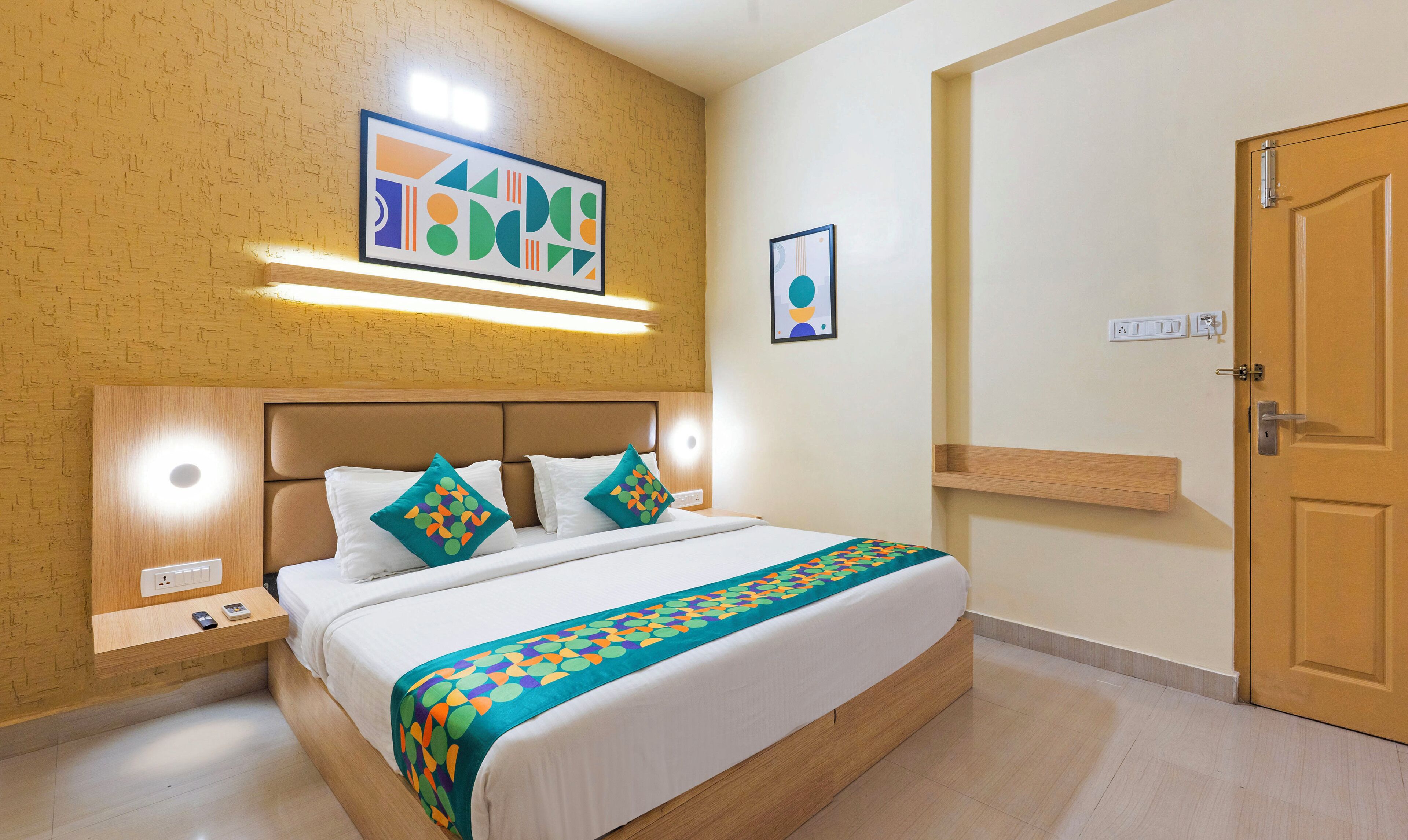 A hotel room with a bed, a nightstand, a wall-mounted light, and a door.