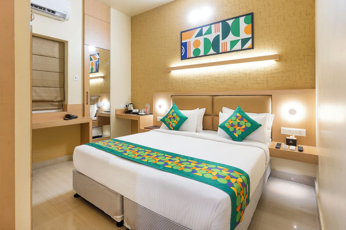 A hotel room with a bed, bedside tables, a mirror, a wall-mounted artwork, and a window.