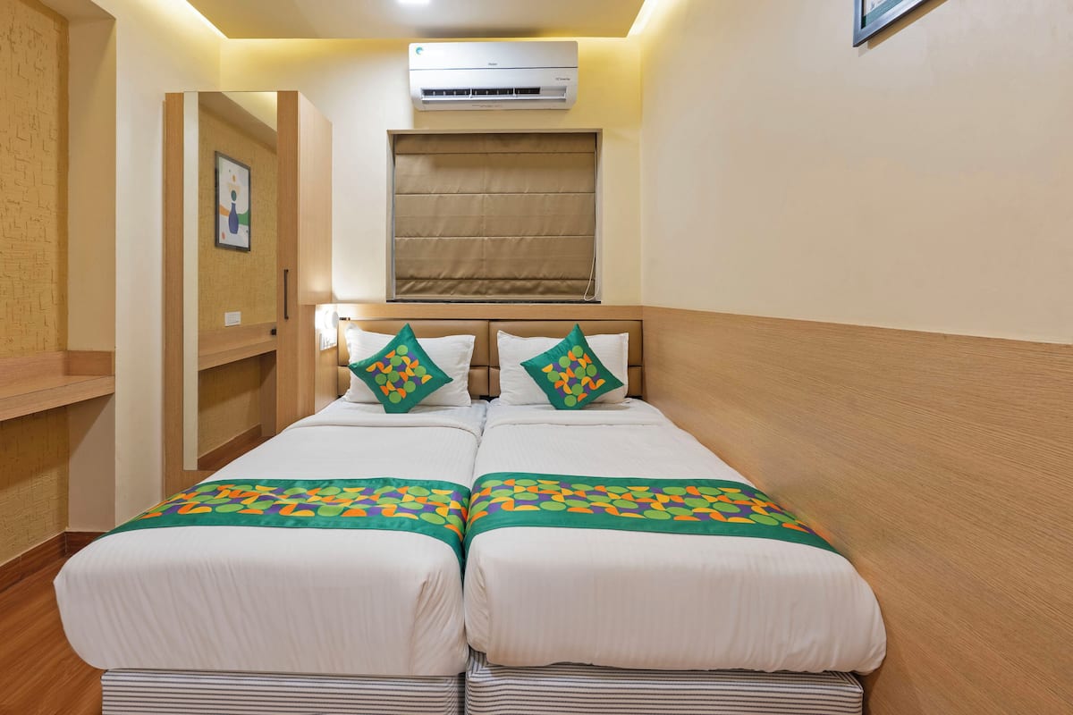 A hotel room with a double bed, an air conditioning unit above the bed, a wooden headboard, and a small shelf.