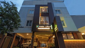 Ein Hotel mit moderner Fassade, Beschilderung mit 'treebo Lijunt' und 'Nestlay Rooms', und ein Auto auf dem Zugangsbereich.