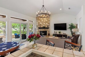 A living room with a stone fireplace, a television mounted on the wall, and a pool table. - Secluded Estate 55 Acres-Pool-Spa-Game Room-Poker Table 5BR 4BA 4 Miles to DT DS (Dripping Springs)