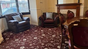 A room with a patterned carpet, a fireplace, a mirror, and two leather chairs.