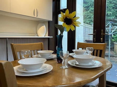 A dining table set with white bowls and wine glasses, a vase with a sunflower, and a view of greenery outside.. Amazing Entire Home in Wolverhampton