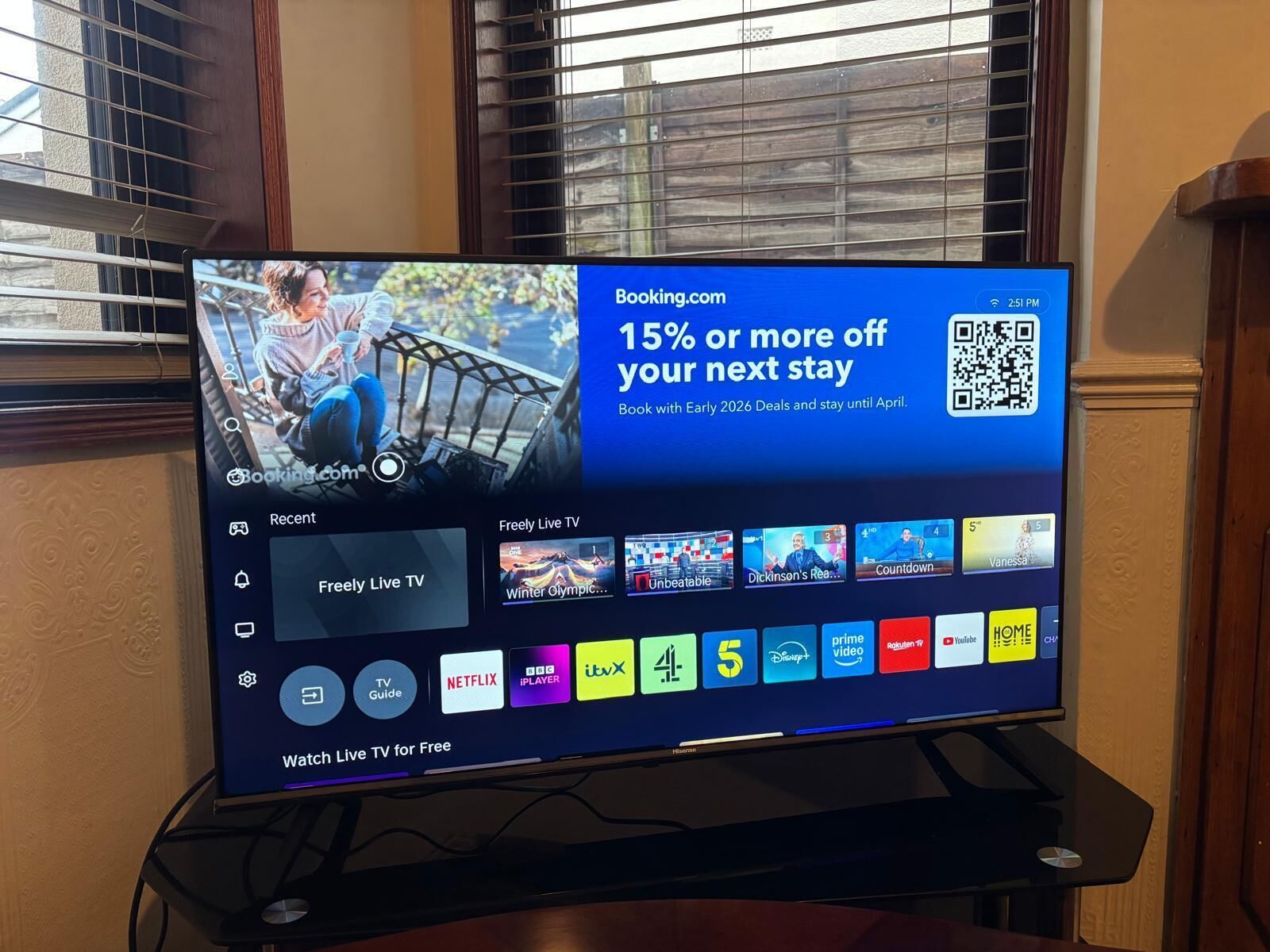 Un televisor mostrando un anuncio de Booking.com con un descuento del 15% en una estadía, un código QR y una lista de canales de televisión.