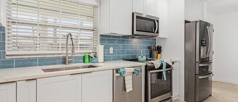 A modern kitchen with white cabinets, a stainless steel refrigerator, a microwave, and a tiled backsplash.