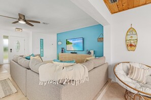 Uma sala de estar com um sofá, uma televisão e um prancha de surf fixada na parede.