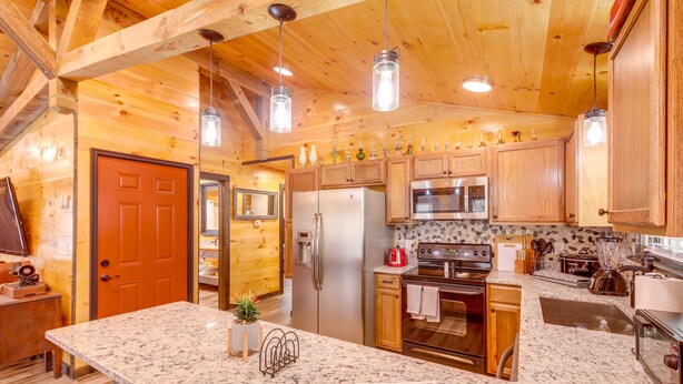 Une cuisine spacieuse dotée de meubles en bois, de plans de travail en granit, d’appareils électroménagers en acier inoxydable et de luminaires suspendus.