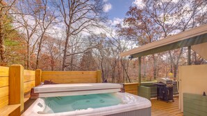 Un bain à remous sur une terrasse en bois, avec un espace couvert et un barbecue à l’arrière-plan.