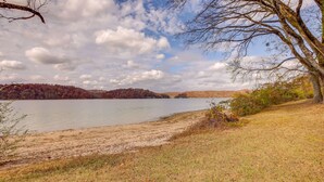 Une vue sur le lac, avec une zone herbeuse, des arbres et une colline au loin.