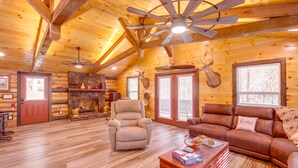L’intérieur d’une cabane en rondins, avec une cheminée, un fauteuil inclinable, un canapé et des bois de cerf accrochés au mur.