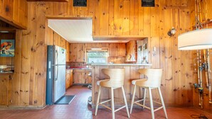 Une cuisine avec des murs en bois, un réfrigérateur, un évier et deux tabourets de bar.