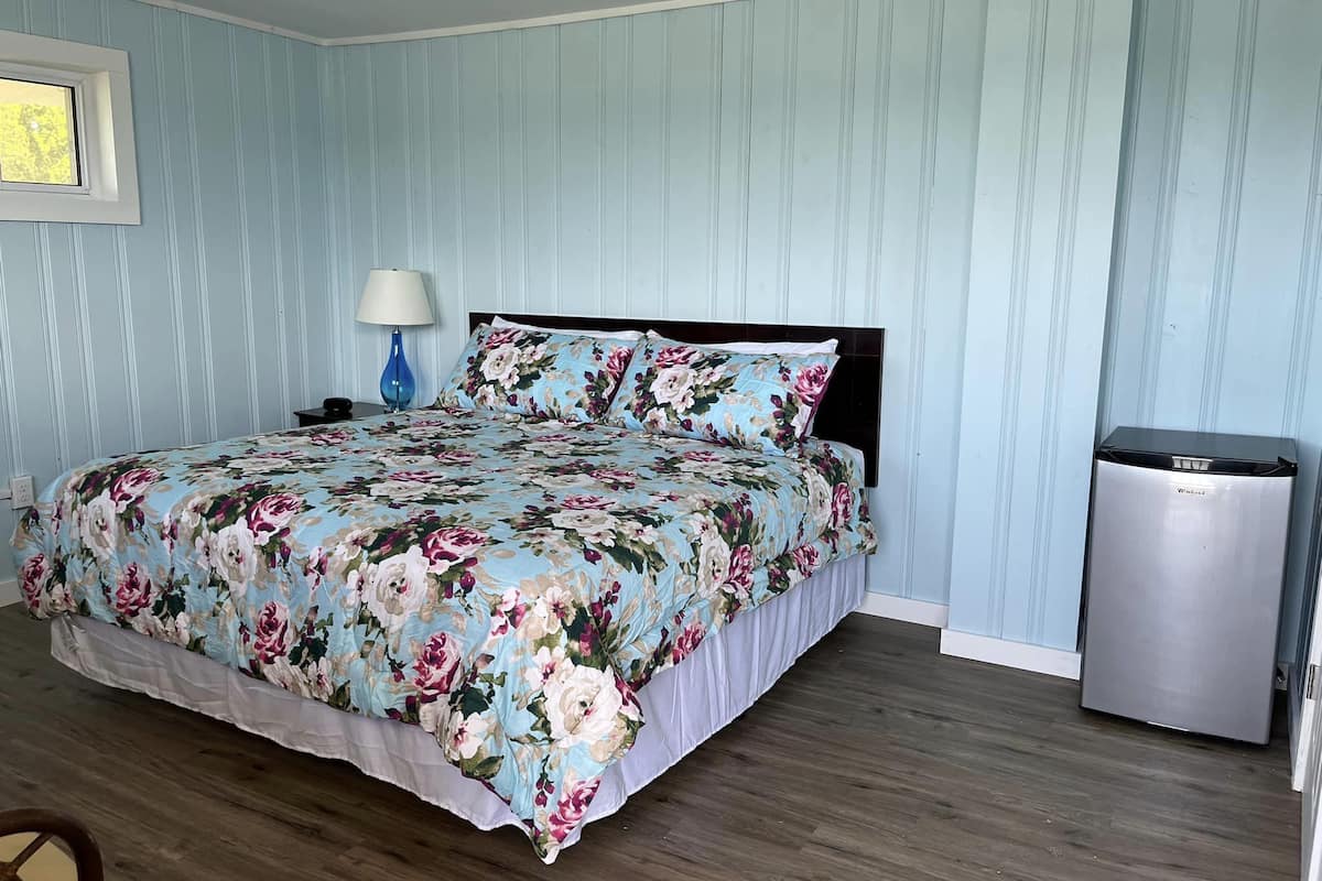 A bedroom with a floral bedspread, a bedside lamp, and a compact refrigerator.