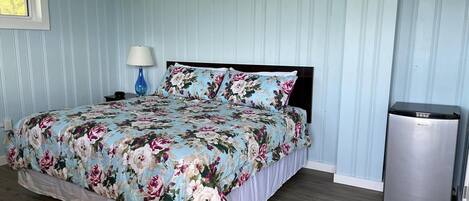 Een slaapkamer met een bloemenbedekker, een bedlampje en een compacte koelkast.