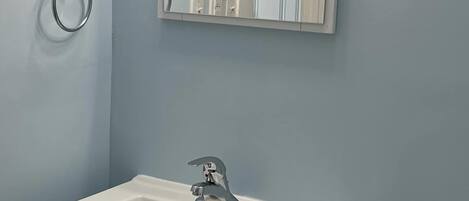A bathroom with a white sink, a mirror with lights above it, and a towel ring on the wall.