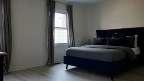 Un dormitorio con cama, mesita de noche y ventana con cortinas.
