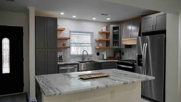 Una cocina moderna con gabinetes grises, electrodomésticos de acero inoxidable y encimera de mármol.
