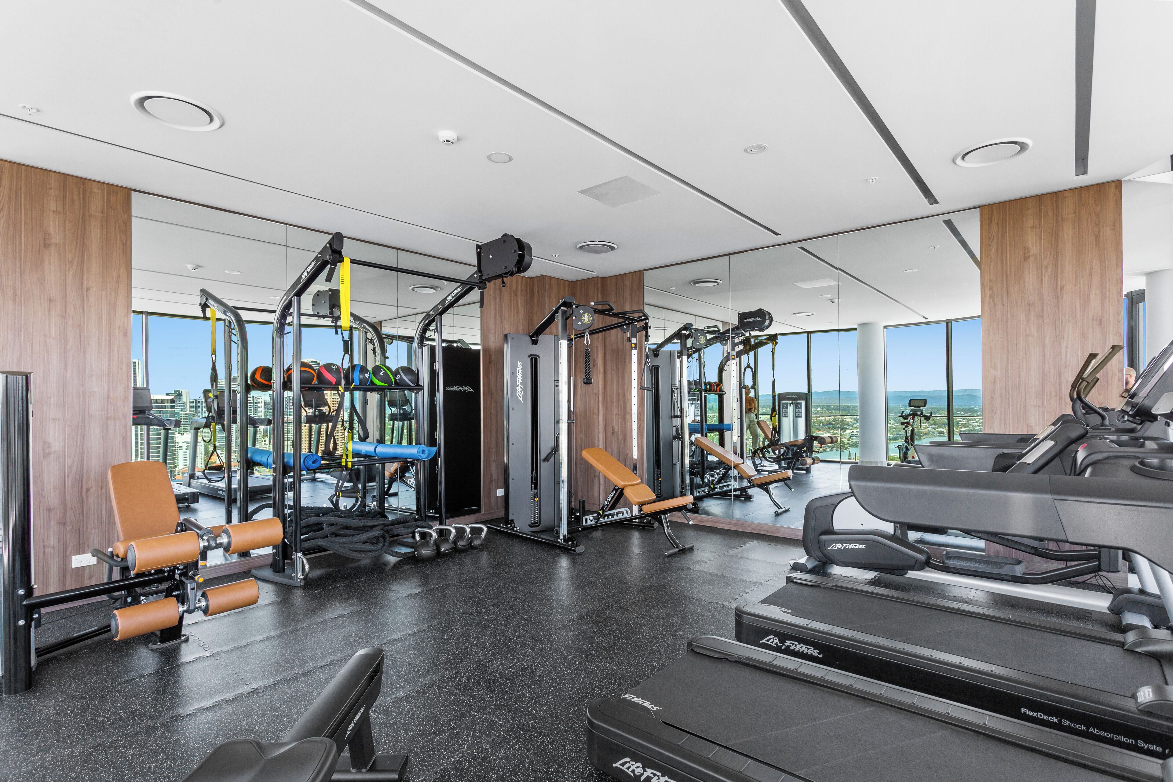 Un gimnasio moderno con diversos equipos de ejercicio, ventanas amplias y vista a la ciudad.