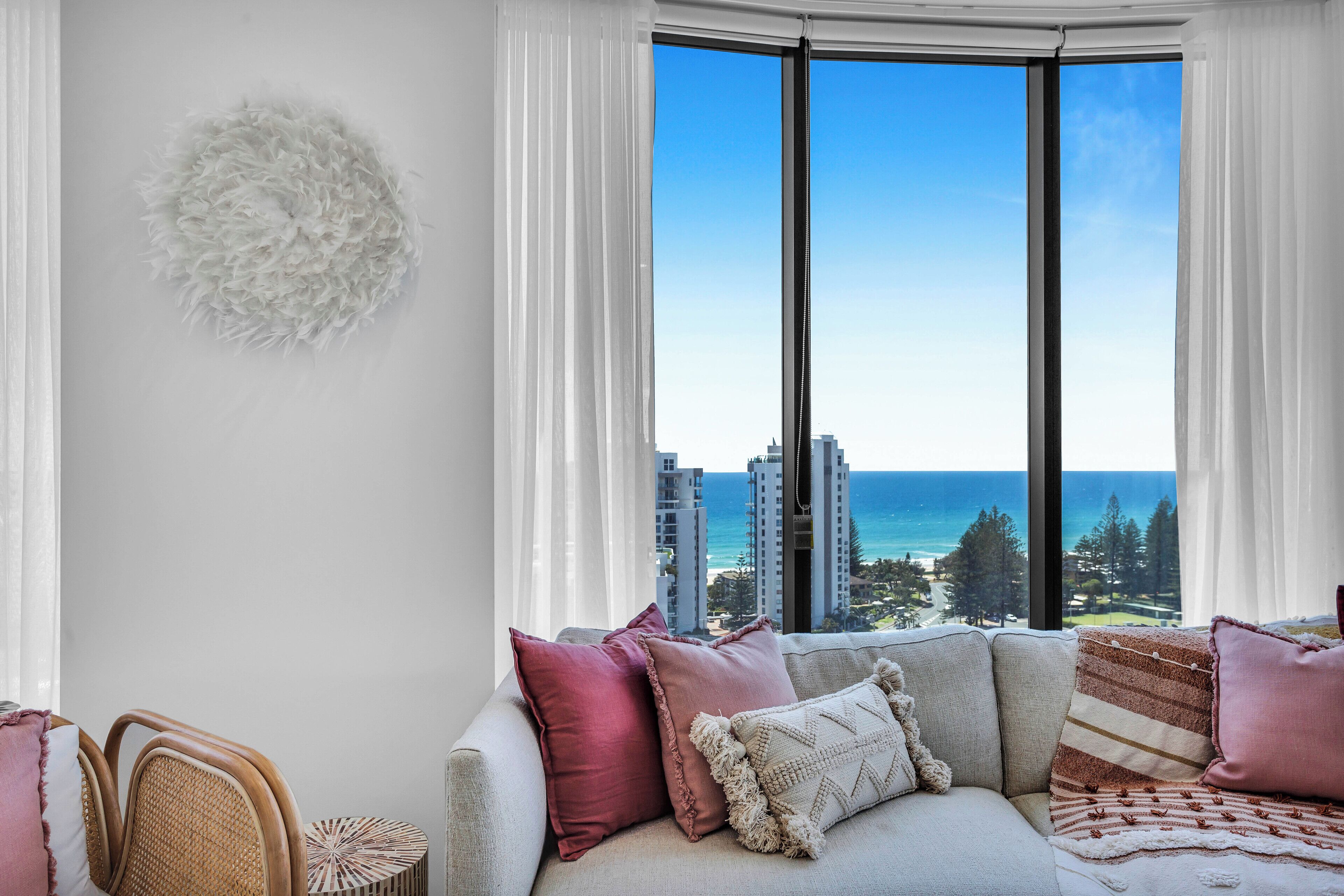 A modern living room with a large window offering a view of the ocean and high-rise buildings.