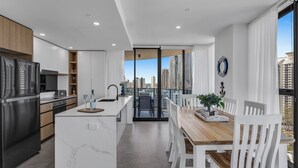 Eine moderne Küche mit einer zentralen Kochinsel, einem Essbereich mit weißen Stühlen und Blick auf die Stadt durch große Fenster.