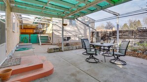 Un'area patio coperta con tavolo e sedie, un cesto appeso e una recinzione in legno sullo sfondo.