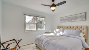 Una camera da letto con un letto, una ventola a soffitto, una finestra e un quadro appeso al muro.