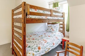 Una cama litera con ropa de cama floral, una silla de madera y una ventana con cortinas.