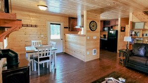 Ein gemütliches Blockhaus-Interieur mit Essbereich, Wohnzimmer mit Ledersofa, Küche mit Holzschränken und einer Treppe.