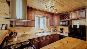 Eine Küche mit Holdekor-Schränken, einer Edelstahl-Dunstabzugshaube, einer Arbeitsplatte aus Granit, einer Spüle, einem Herd, einem Kühlschrank und einer Kaffeemaschine.