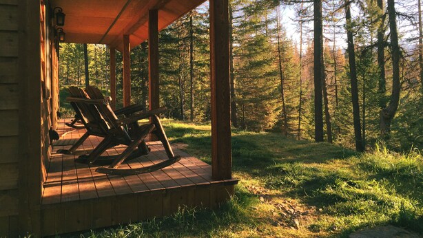 Eine Holzhütte mit Veranda, zwei Schaukelstühlen und Blick auf einen Wald.