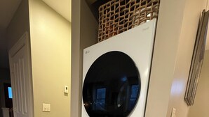 A front-loading washer and dryer unit in a hallway with beige walls and tiled flooring. - North Hill Section Home; walk to UVMMC & UVM, Chabad, downtown, lake. (Burlington)