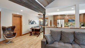Amplia sala de estar con una mesa de comedor de madera, un sofá moderno y una cocina con armarios de madera y electrodomésticos de acero inoxidable.