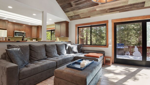 Una sala de estar moderna con un sofá seccional, un reposapiés y un comedor con armarios de madera y un microondas.