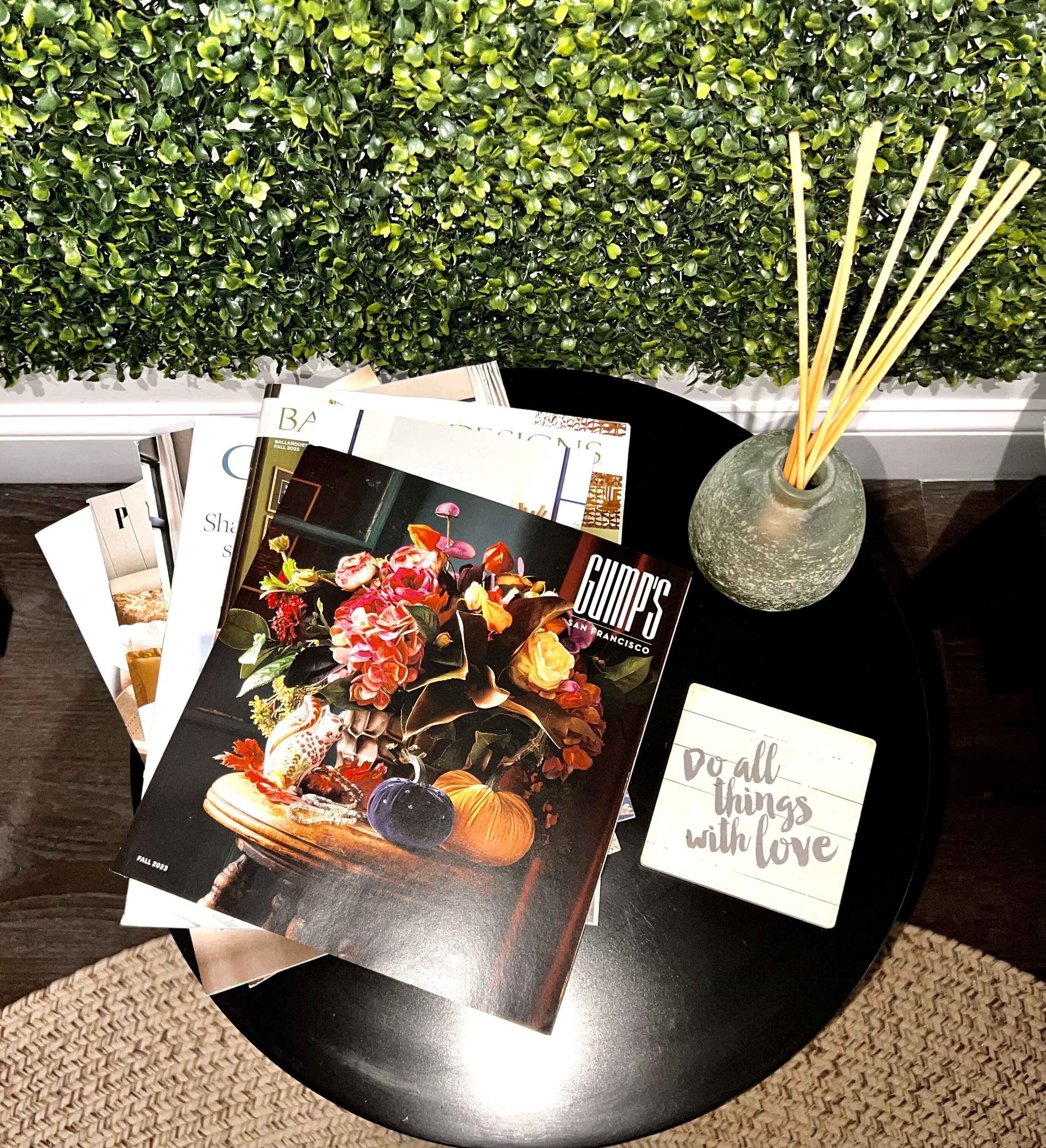 Een tafel met tijdschriften, een decoratieve vaas met takken, en een wand met groene beplanting.
