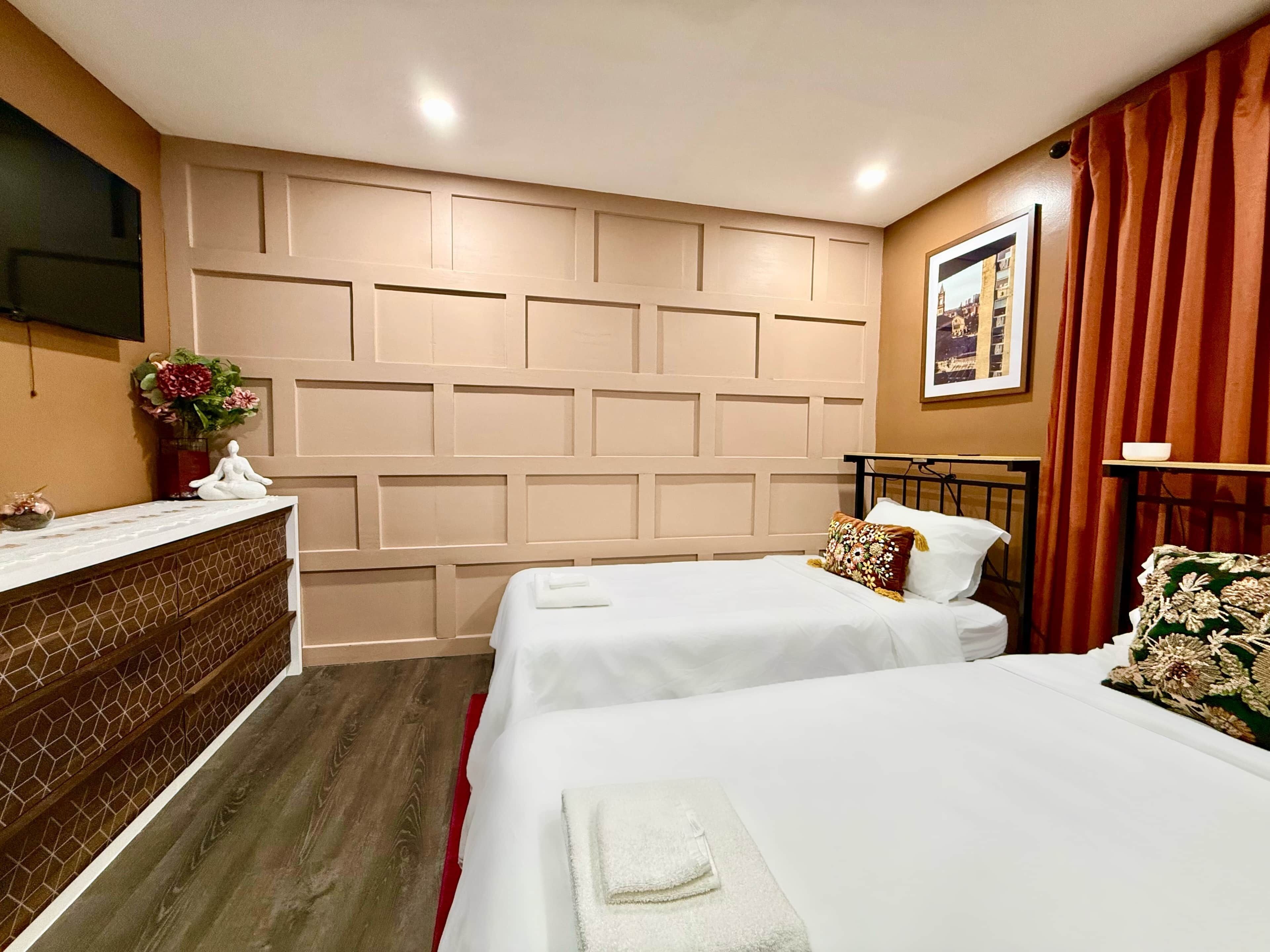 Une chambre d’hôtel avec deux lits, un plancher en bois, un téléviseur fixé au mur, une plante en pot et un tableau encadré.