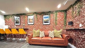 A room with a brick wall, a brown leather sofa with patterned cushions, and yellow chairs. - Serenity Suite Homes 2BD/1BA near Logan Intl/Metro (Boston)
