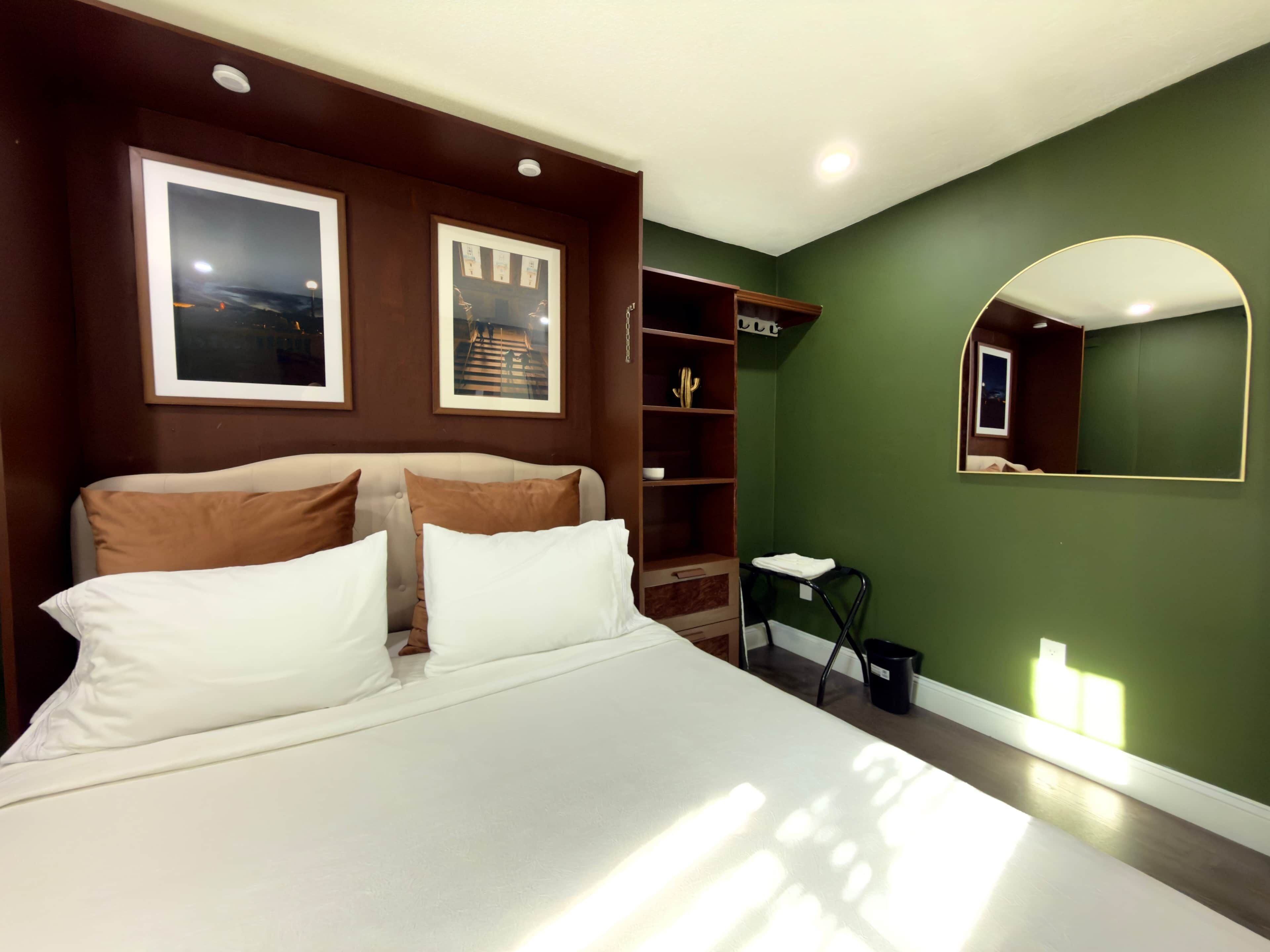 A modern bedroom with a large bed, a built-in wardrobe, a mirror, and framed pictures on the wall.