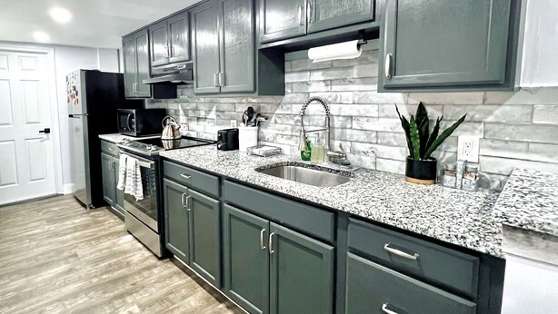 A modern kitchen with dark cabinets, granite countertops, a stainless steel sink, and a microwave. - Serenity Suite Homes 2BD/1BA near Logan Intl/Metro (Boston)