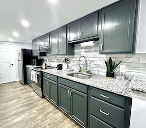 A modern kitchen with dark cabinets, granite countertops, a stainless steel sink, and a microwave.